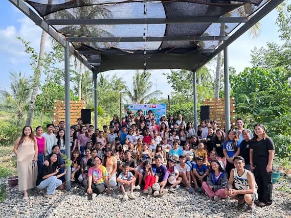 A group of children and adults posing beneath an outdoor pavilion